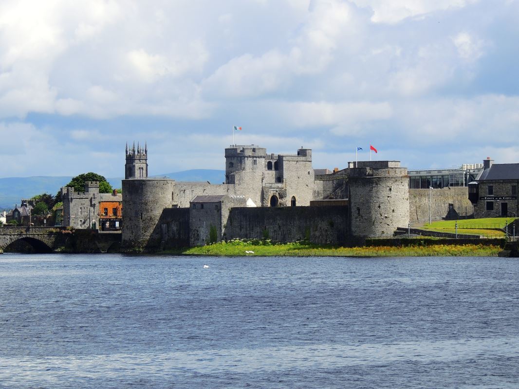 a castle with a large stone wall and a body of water with King John's Castle in the background