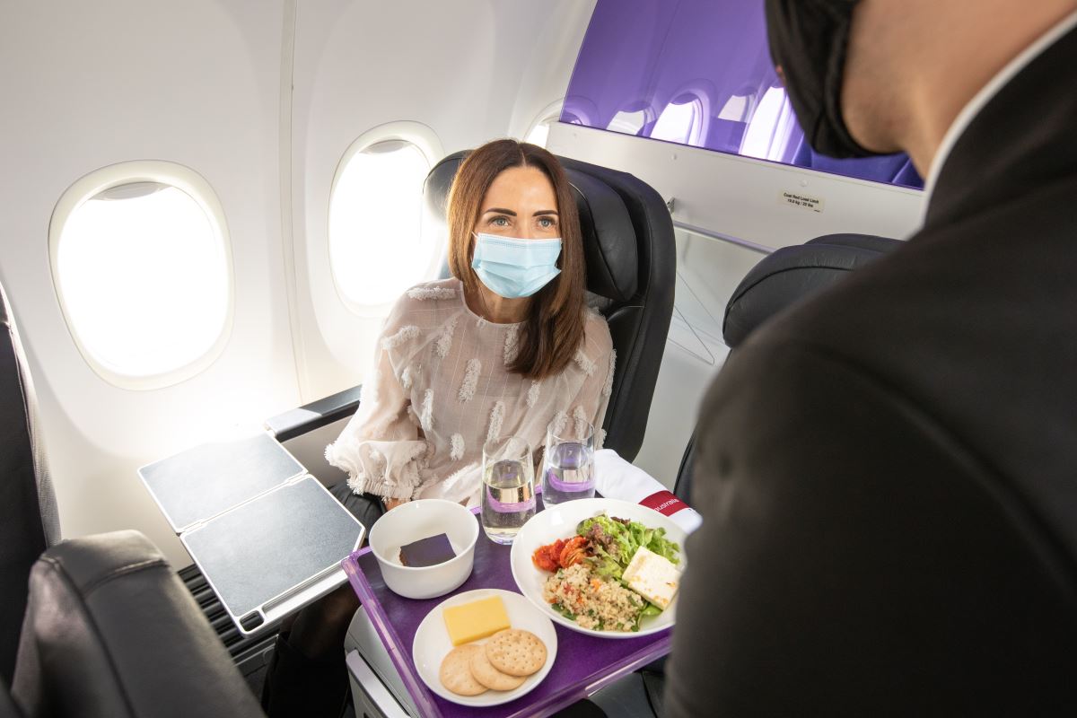 a woman wearing a face mask sitting in a plane with food on a tray