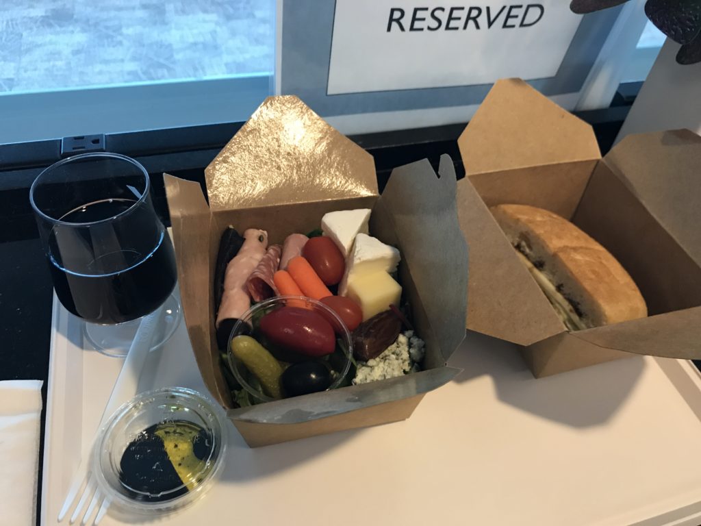 food in a box next to a glass of wine