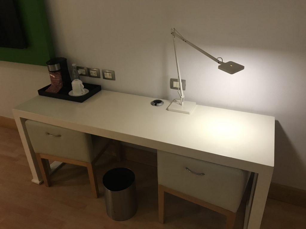 a desk with a lamp and a trash can