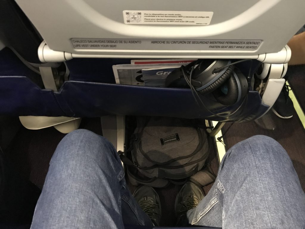 a person's legs and a backpack on the seat of an airplane
