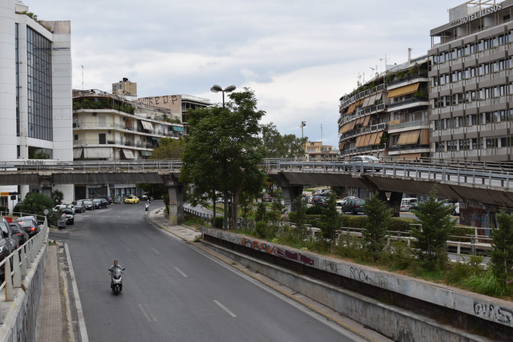 a man riding a motorcycle on a road with buildings and cars