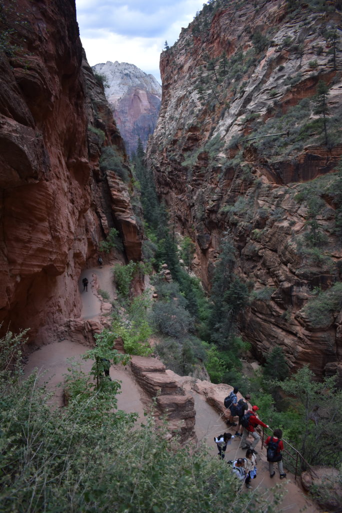 a group of people walking down a narrow canyon with Zion National Park in the background