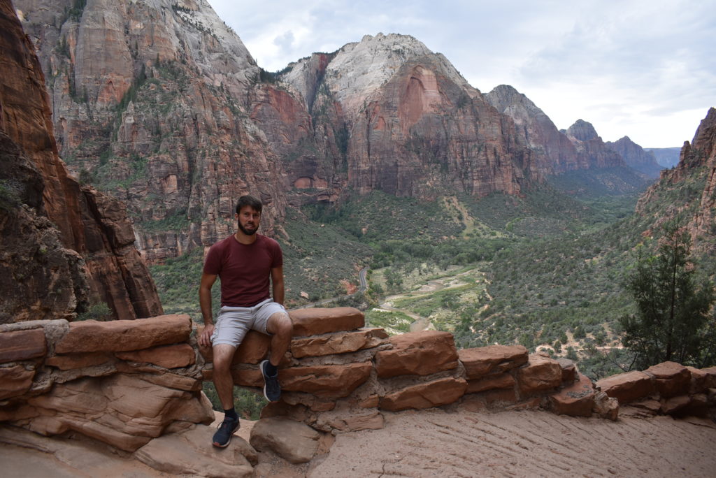 a man sitting on a rock ledge with mountains in the background with Zion National Park in the background