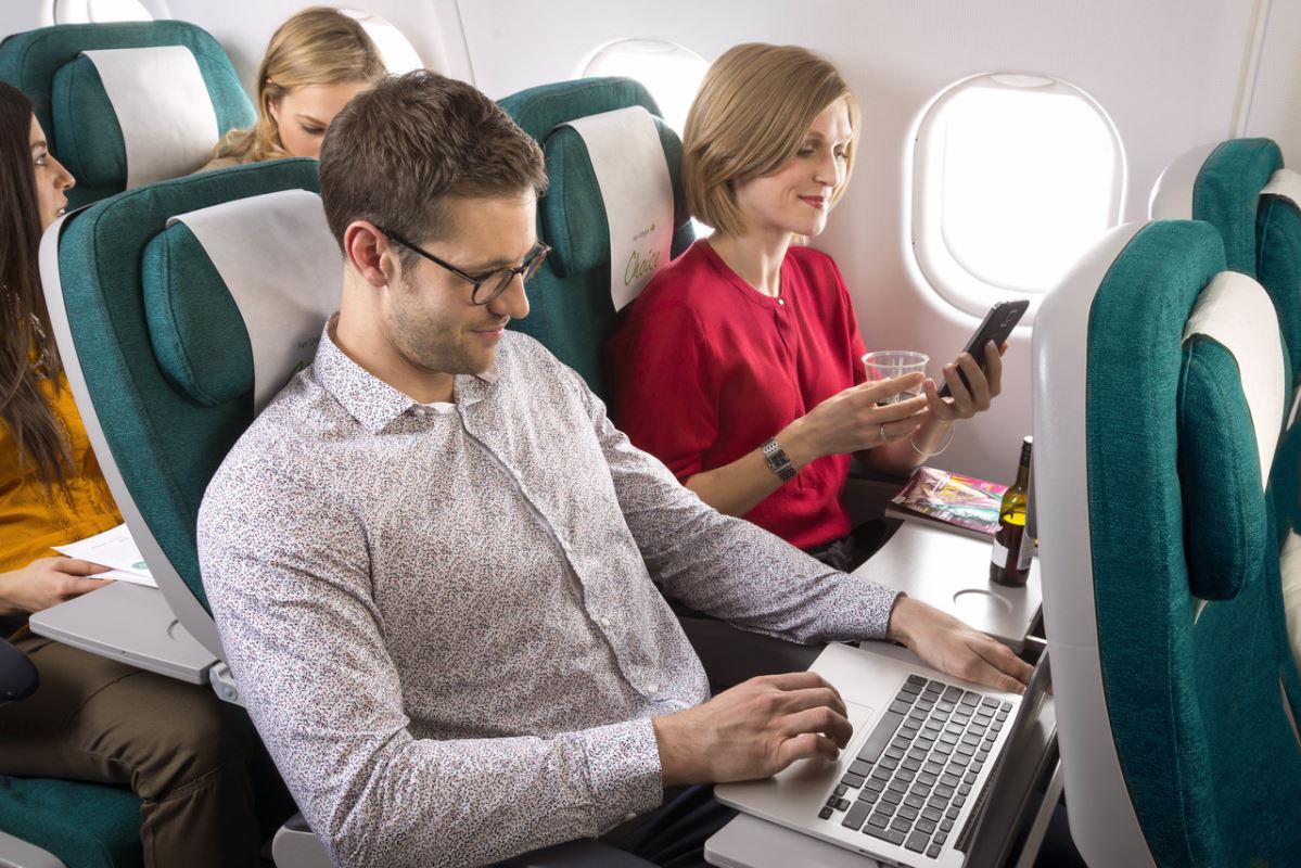 a man and woman sitting on an airplane with a laptop and phone