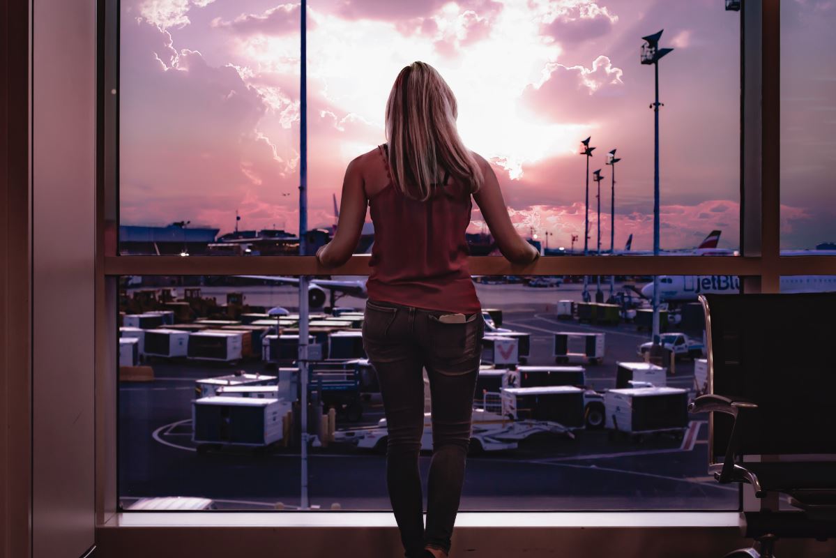 a woman standing in front of a window looking out at a parking lot