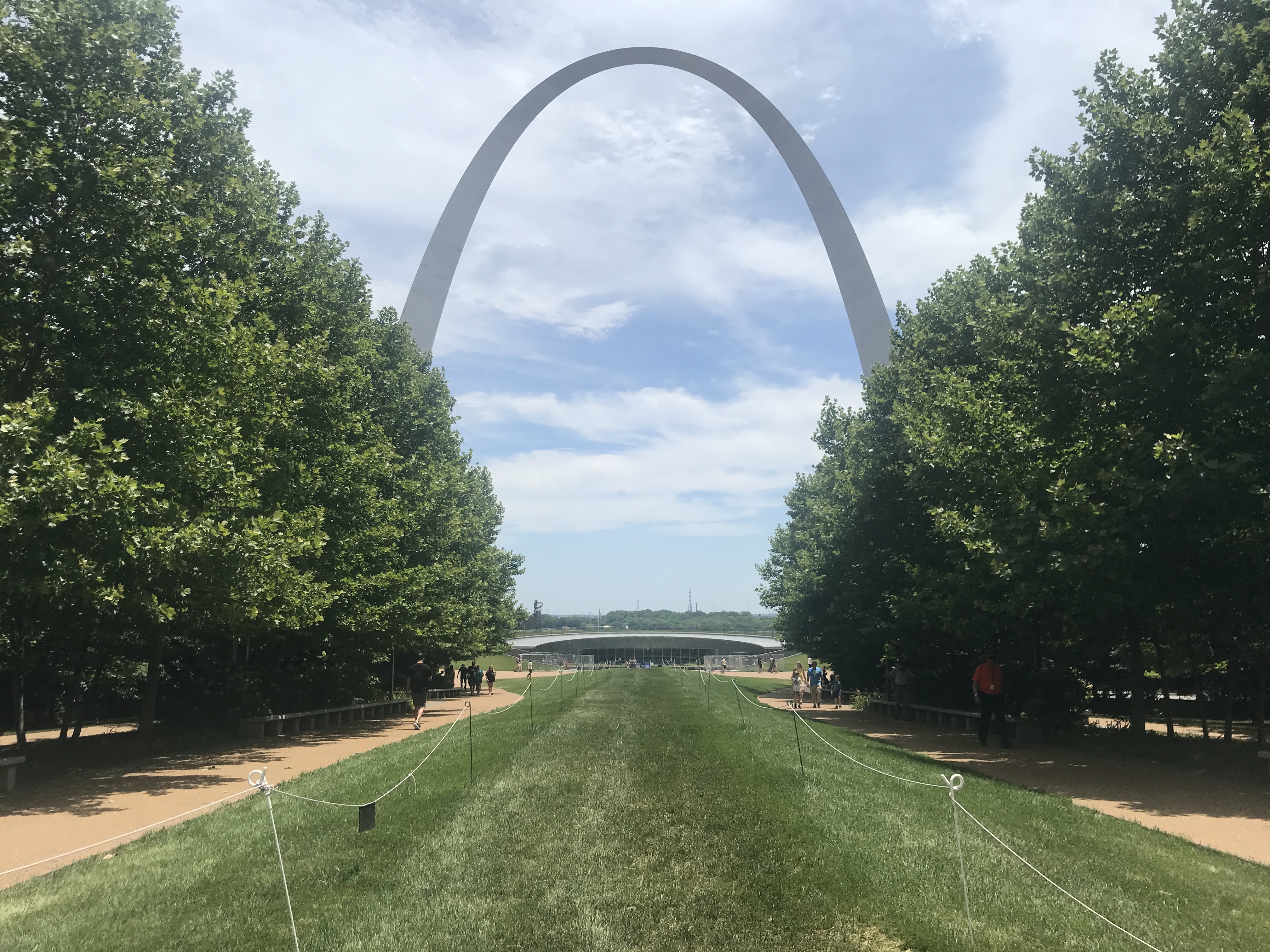 a path with trees and a large arch in the background with Gateway Arch in the background