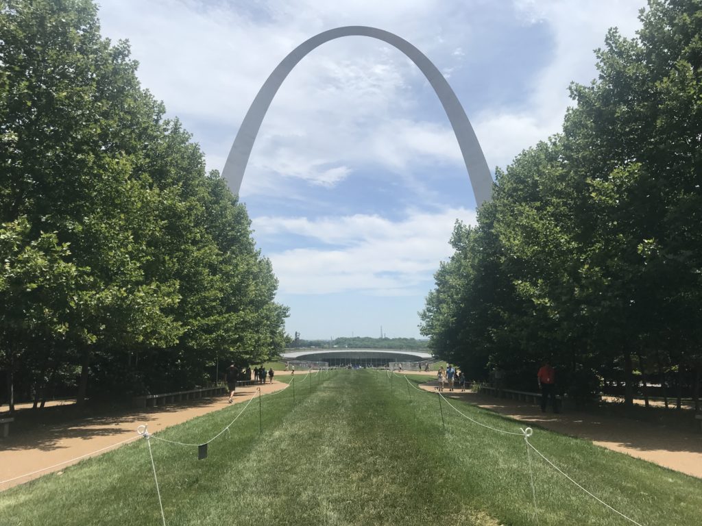 a path with trees and a large arch with Gateway Arch in the background