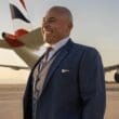 a man in a suit smiling in front of an airplane