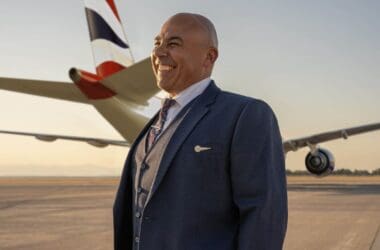 a man in a suit smiling in front of an airplane