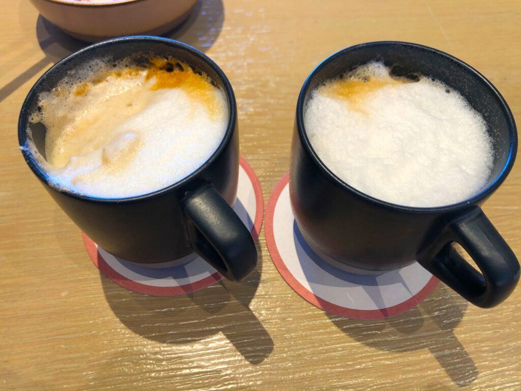 two black mugs with foamy coffee on a table