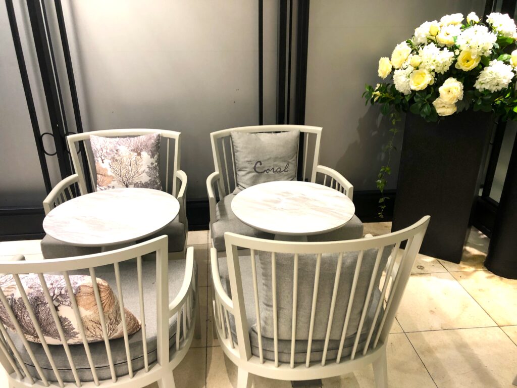 Tables for 4 with a pillow that says Coral on it and the other pillow has a tree with flowers decorating it. White flowers are in the right corner