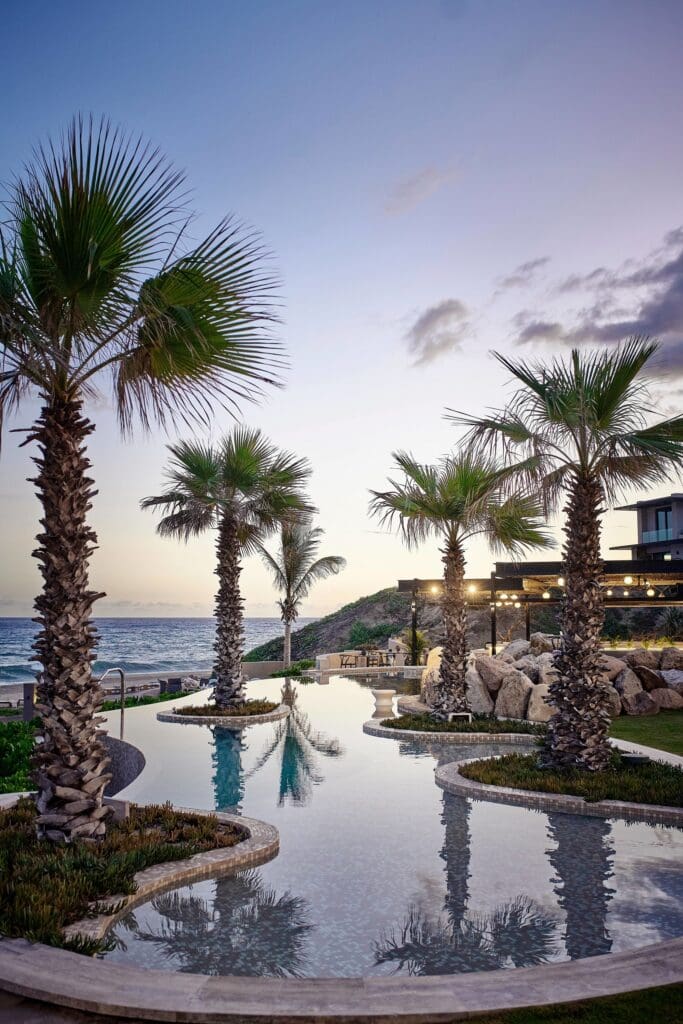 a pool with palm trees and a building on the beach