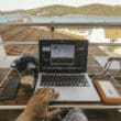 a person using a laptop on a table with a camera and a glass of coffee