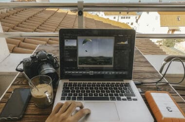 a person using a laptop on a table with a camera and a glass of coffee