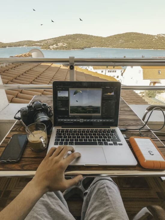 a person using a laptop on a table with a camera and a glass of coffee