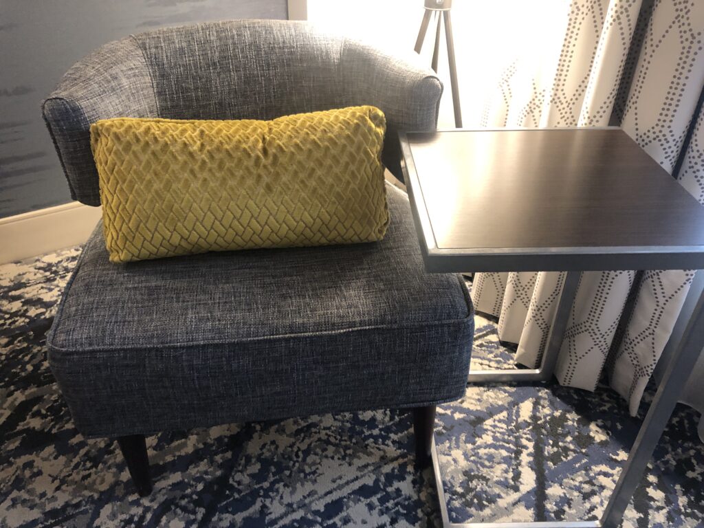 a chair with a yellow pillow next to a table