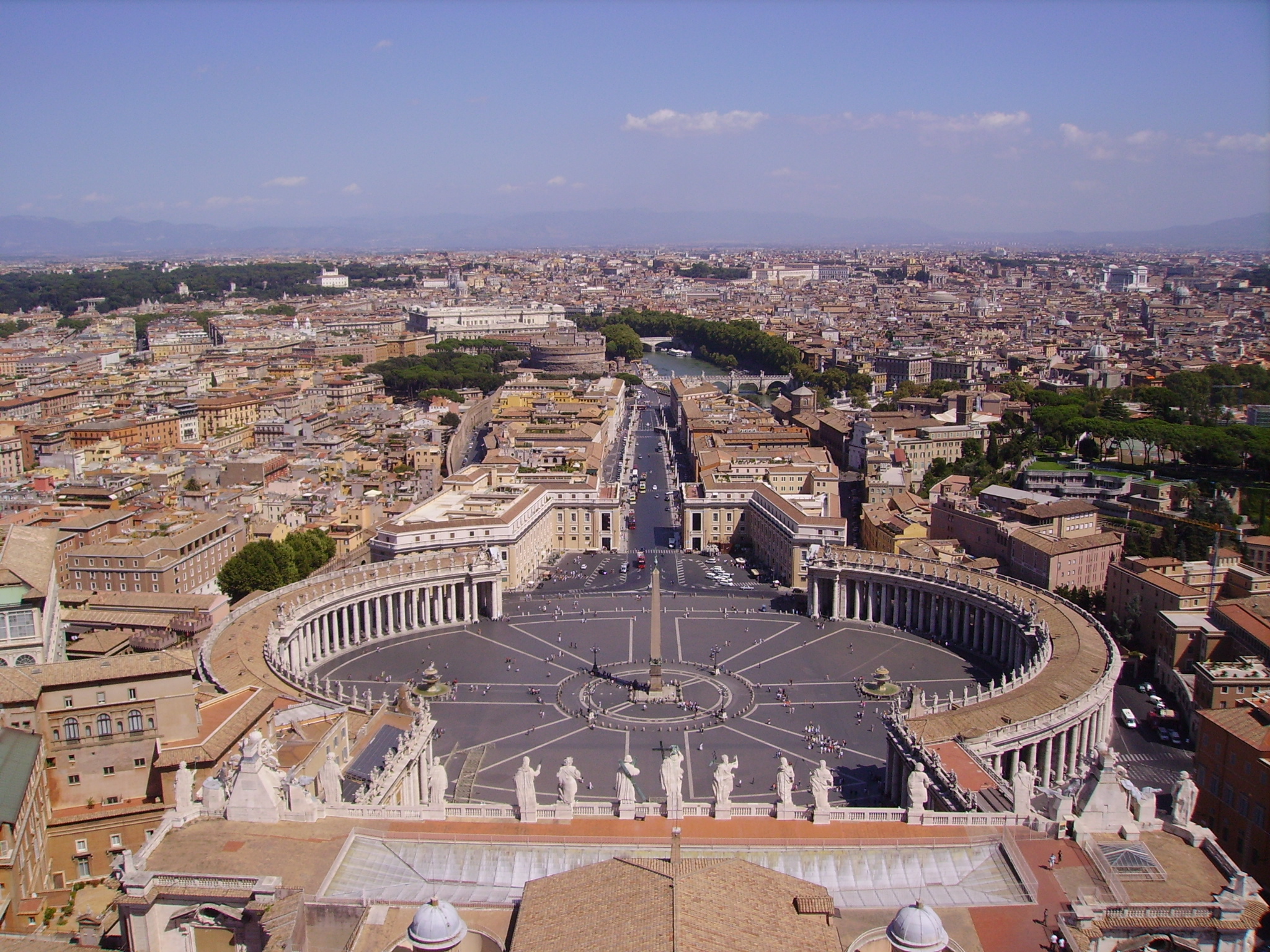 a large circular plaza with columns and a large city with trees with St. Peter's Square in the background