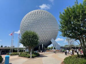a large white sphere with many flags in front of it with Epcot in the background
