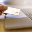 a hand holding a credit card over a laptop