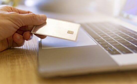 a hand holding a credit card over a laptop