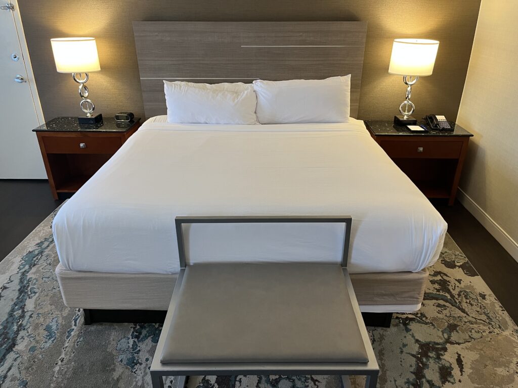 a bed with white sheets and a bench with two lamps