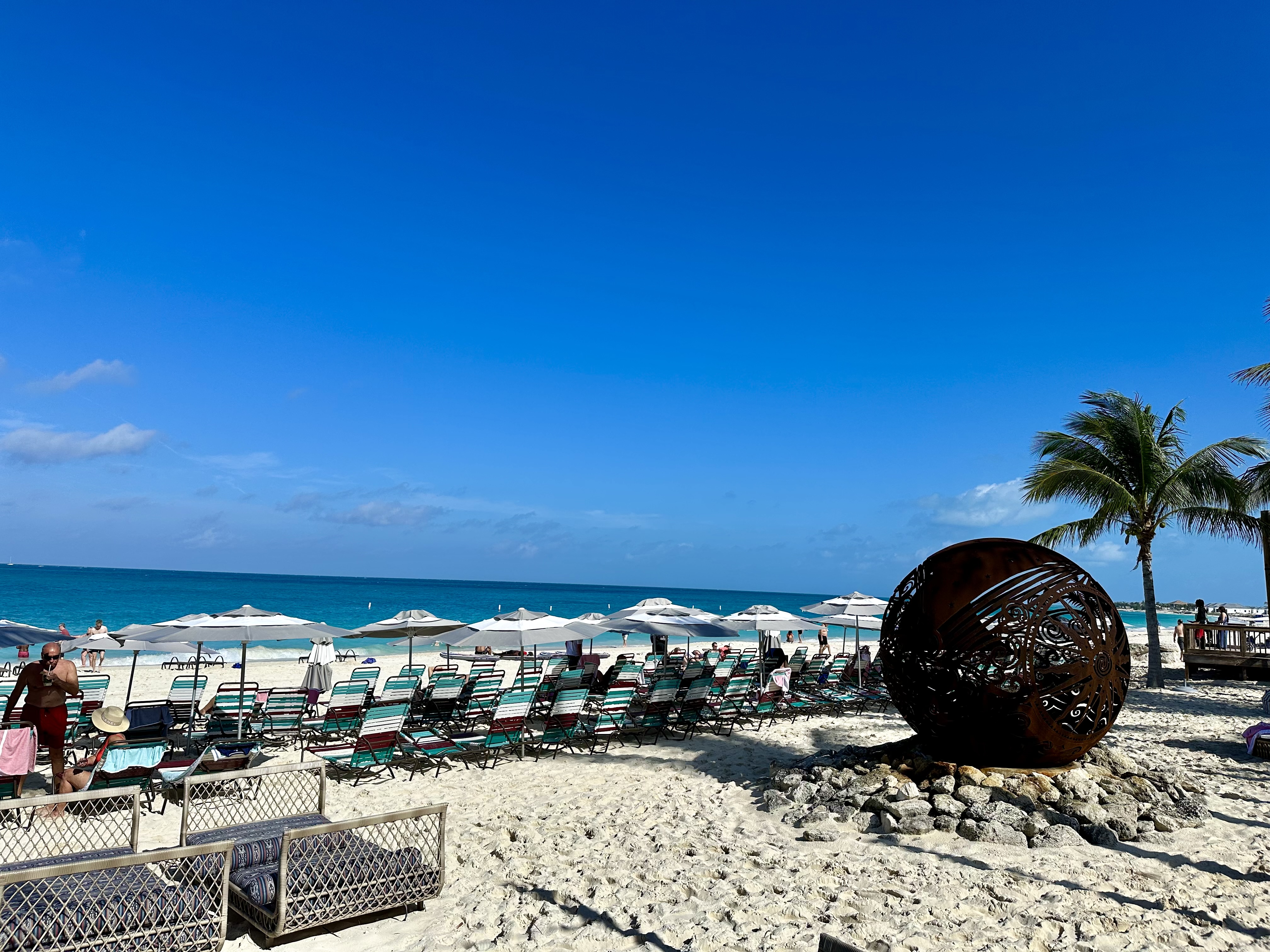 a beach with a large metal ball and palm trees