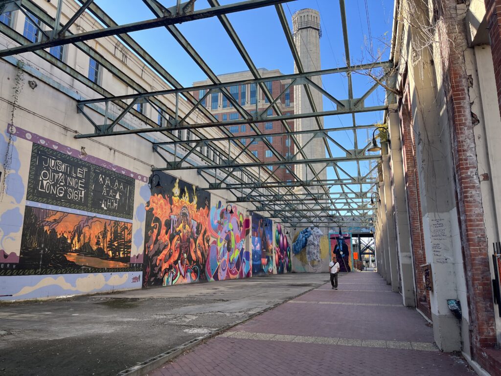 a person walking down a walkway with a mural on the wall