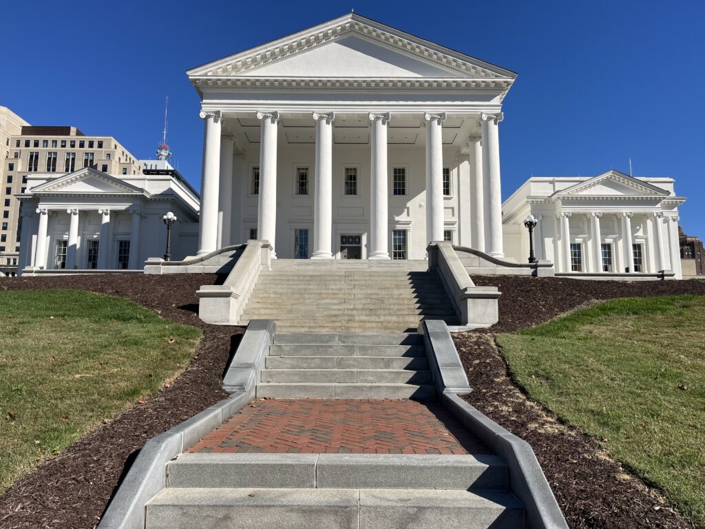 a white building with columns with Virginia State Capitol in the background