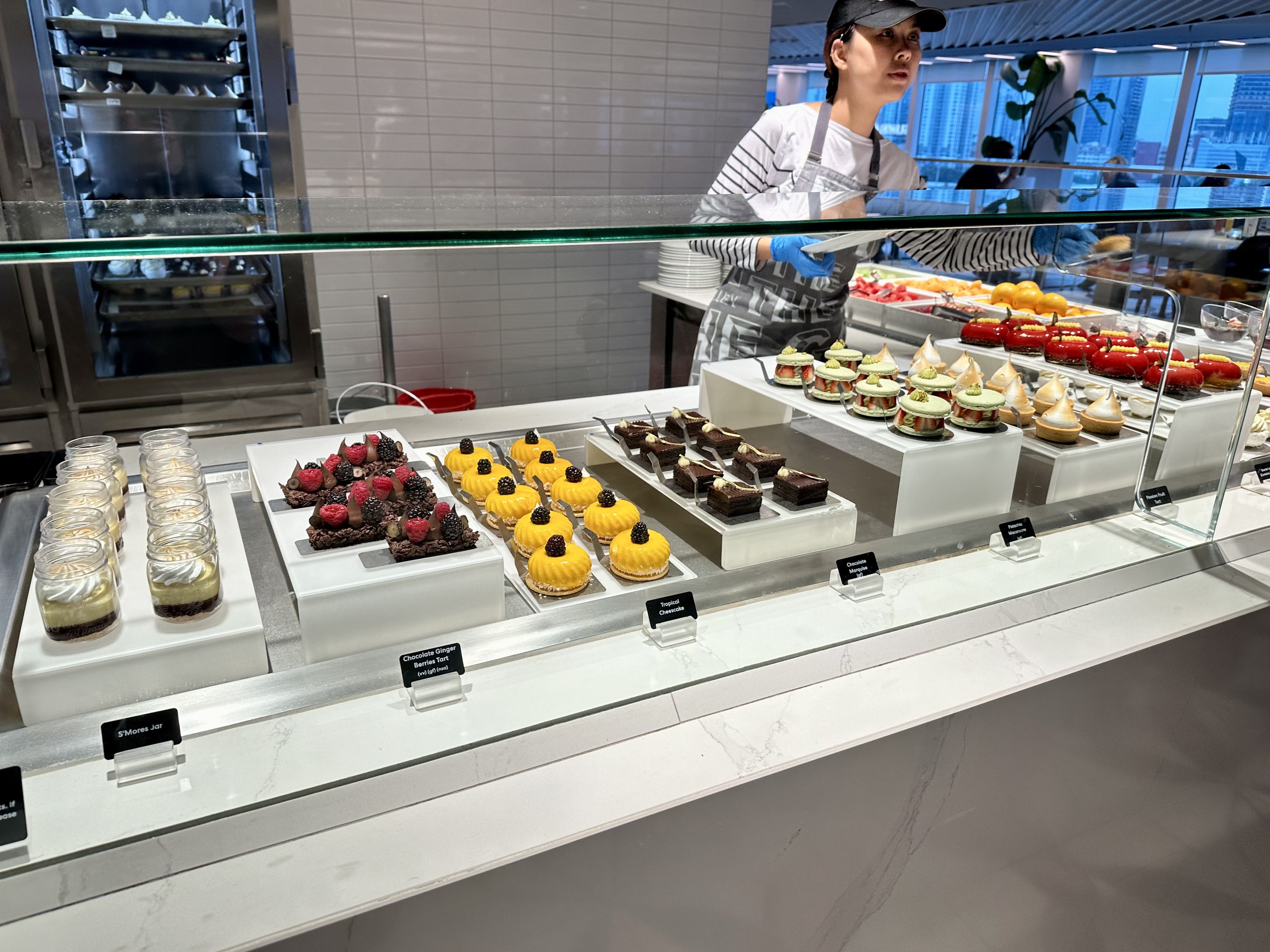 a person standing behind a display case of desserts