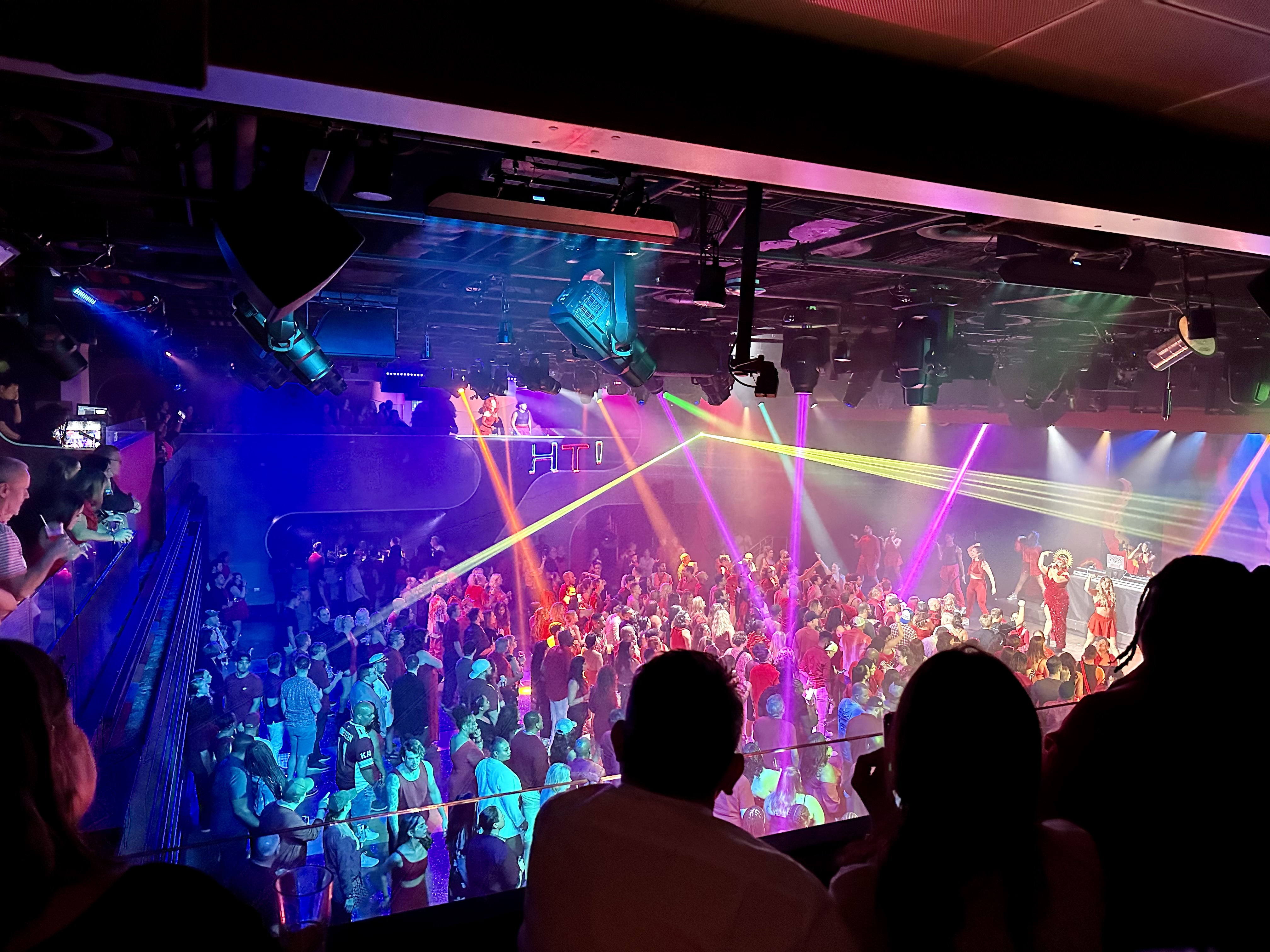 a crowd of people in a room with lights and a stage on Virgin Voyages Scarlet Lady
