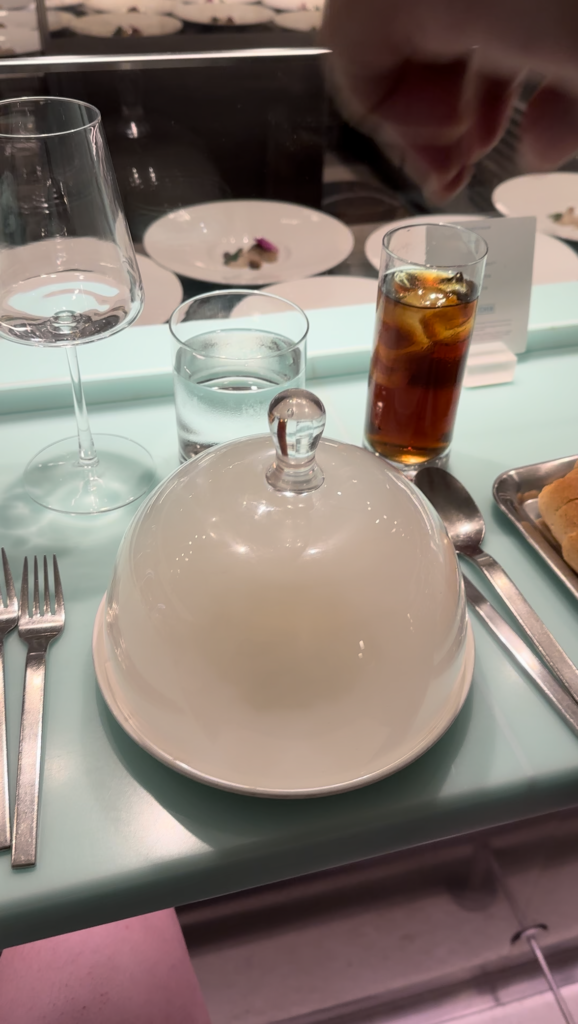 a plate with a lid and glasses of liquid and silverware on a table