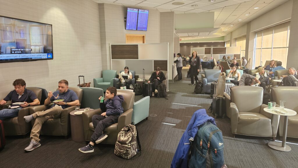 people sitting in chairs in a room with people waiting for their flight