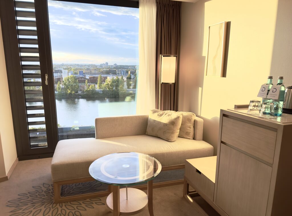 The sitting room in a hotel room with ottoman and window overlooking the Main River.