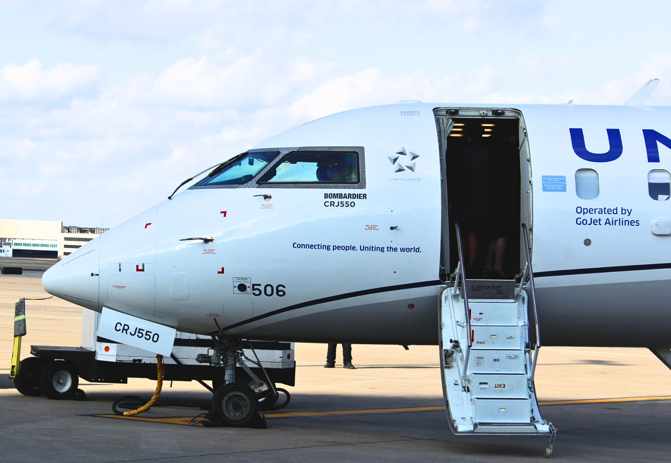 A United Express Bombardier CRJ-550 parked on the ramp with the main boarding door open.