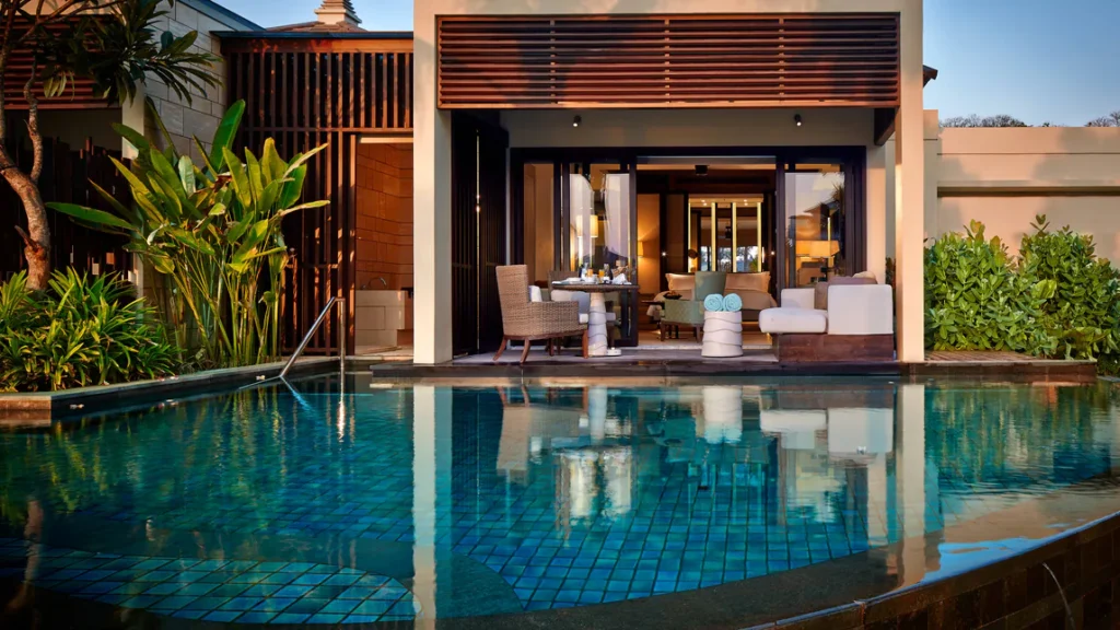 An exterior view of a pool with a table and chairs in front of a room at the Ritz-Carlton Bali