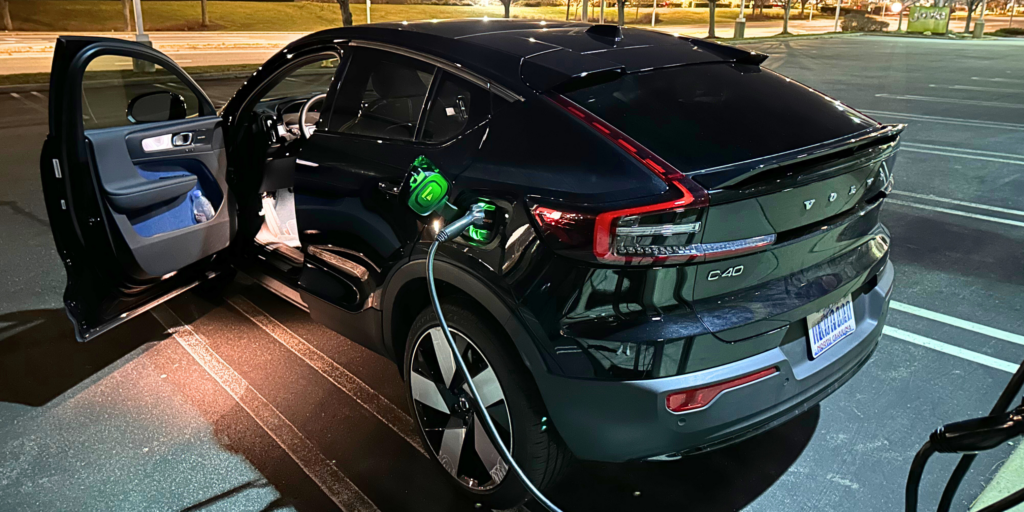 A black electric car at a charging station with charger attached to the vehicle.
