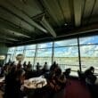 a group of people sitting at tables in a room with large windows at the Aspire Lounge Helsinki.