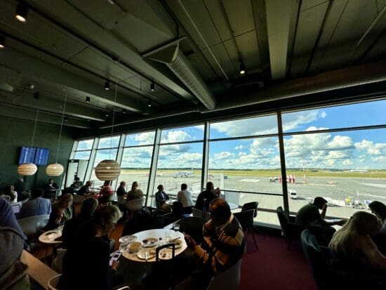 a group of people sitting at tables in a room with large windows at the Aspire Lounge Helsinki.