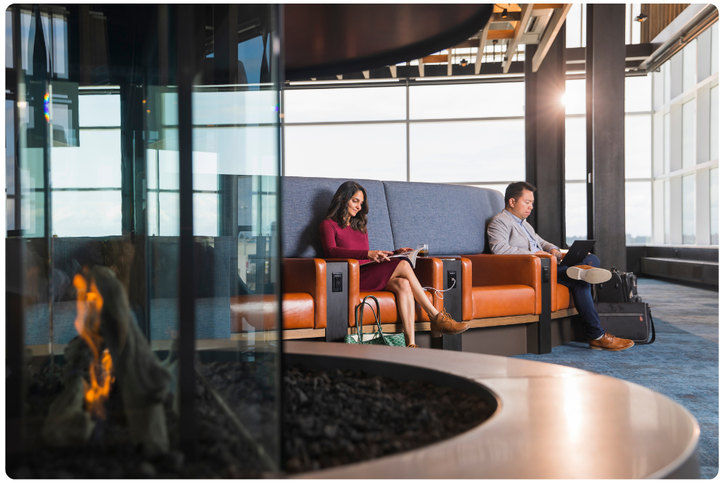 Two passengers sit in an Alaska Airlines Alaska Lounge near a fireplace