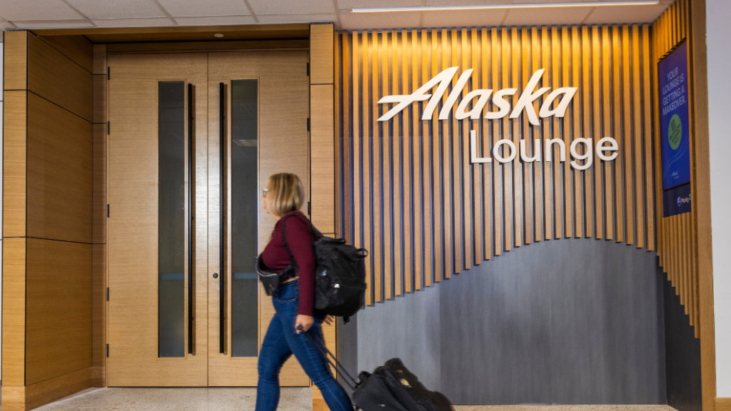 A woman walking past an Alaska Lounge, an Admirals Club partner lounge location