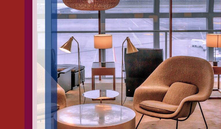 An airport lounge with upscale furniture including chairs and tables next to an assortment of colored bars that serve as decorative accents