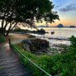 a wooden walkway leading to a beach with a boat in the water