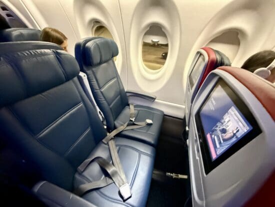 seats in a Delta Airlines A220 with a screen and a monitor