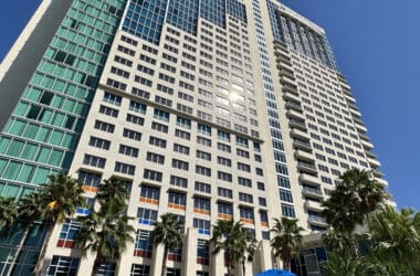 a tall building with palm trees and blue umbrellas