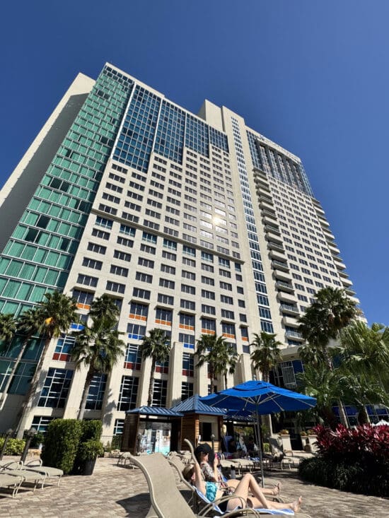 a tall building with palm trees and blue umbrellas