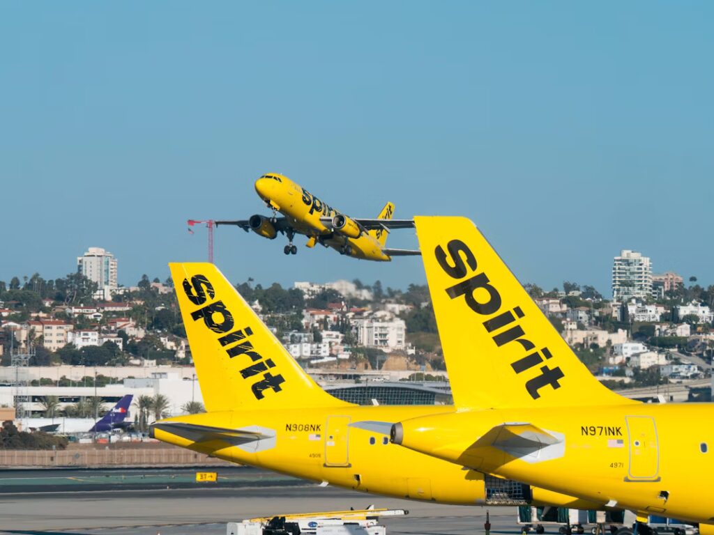Spirit Airlines aircraft parked at the gate as another Spirit Airlines aircraft takes off in the background
