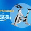 An image of a Peloton-like stationary bike on a gradient blue background accompanied by text to the left that reads "Upgraded to a Peloton Wellness Room"