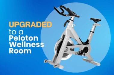 An image of a Peloton-like stationary bike on a gradient blue background accompanied by text to the left that reads "Upgraded to a Peloton Wellness Room"