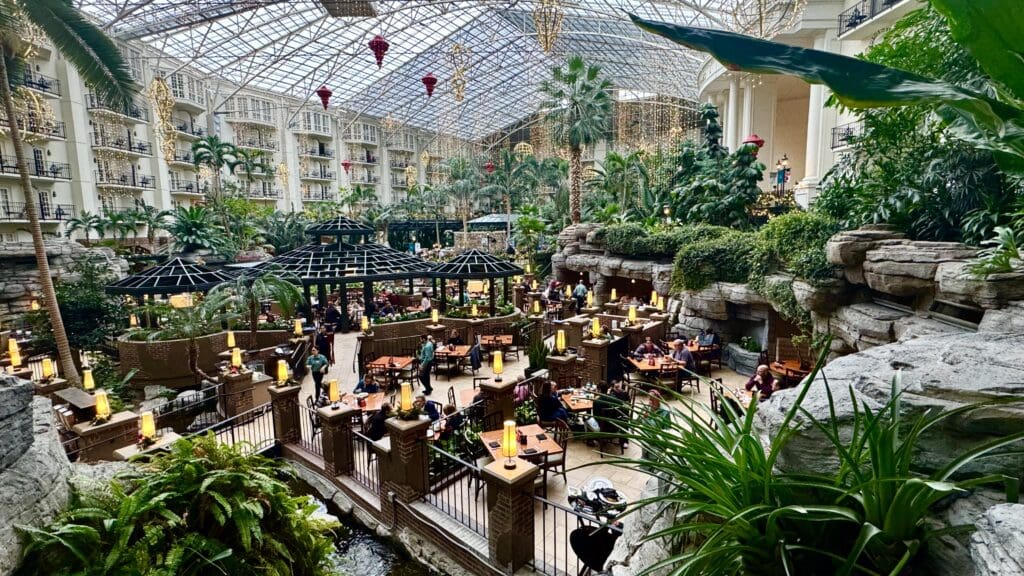 a large indoor restaurant with many tables and plants with Gaylord Opryland Resort & Convention Center in the background